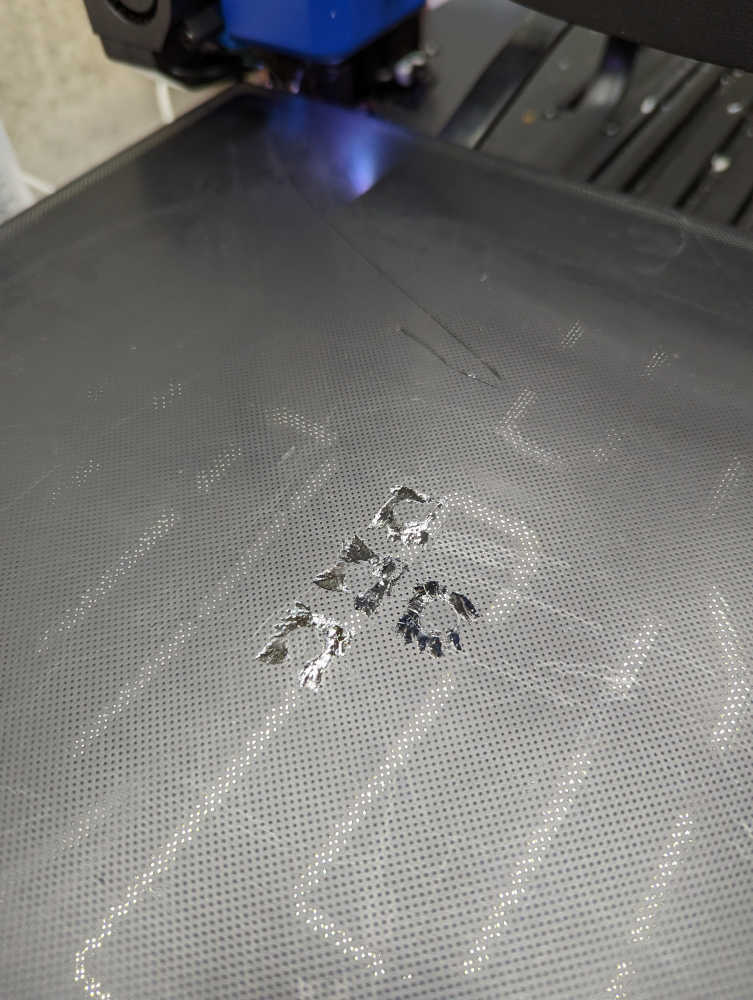 A picture of the 3D printer bed with chips in it from the overly-adhesive PETG print